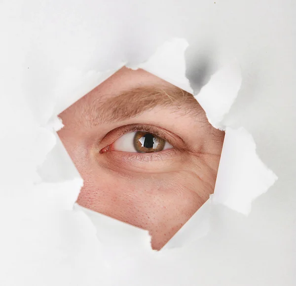 Man eye looking through hole in sheet of paper — Stock Photo, Image