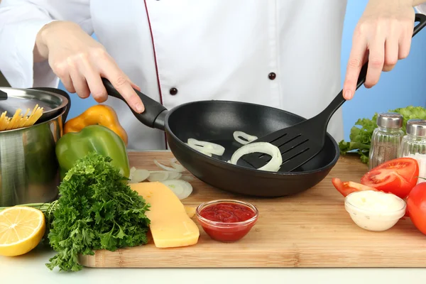 Les mains préparent l'oignon sur la casserole, sur fond bleu — Photo