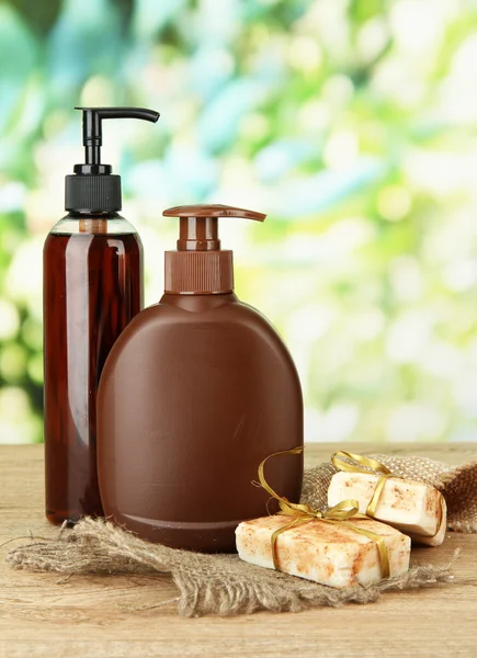 Liquid and hand-made soaps on wooden table, on green background — Stock Photo, Image