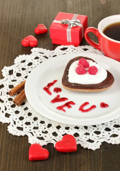Шоколадное печенье в форме сердца с чашкой кофе на деревянном столе крупным планом — стоковое фото