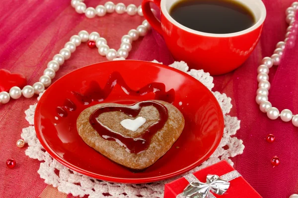 Schokoladenkeks in Herzform mit Tasse Kaffee auf rosa Tischdecke in Großaufnahme — Stockfoto