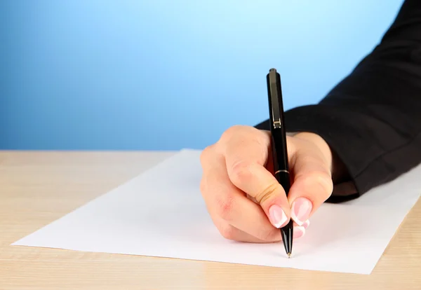 Hand with pen on white paper, on wooden table on blue background Stock Image