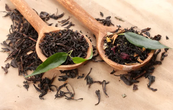 Té seco con hojas verdes en cucharas de madera, sobre fondo de madera — Foto de Stock