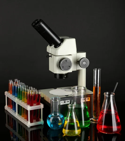 Tubes à essai avec liquides colorés et microscope sur fond gris foncé — Photo