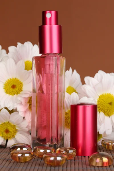 Vrouw perfume in mooie fles met camomiles op bruine achtergrond — Stockfoto