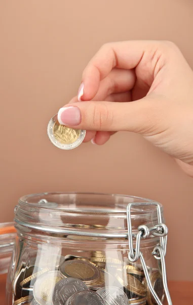 Sparen, weibliche Hand steckt eine Münze in Glasflasche, auf farbigem Hintergrund — Stockfoto