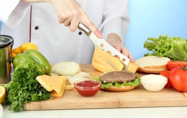 Mani femminili che preparano cheeseburger, su sfondo blu — Foto Stock