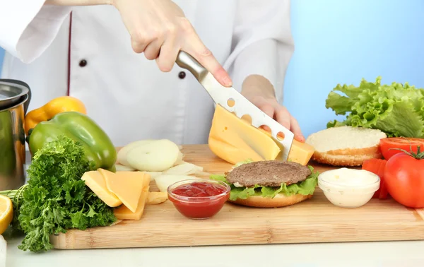 Female hands preparing cheeseburger, on blue background — Stock Photo, Image