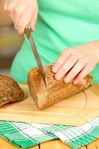 Женщина нарезает хлеб семенами кунжута на доске на деревянном столе. — стоковое фото