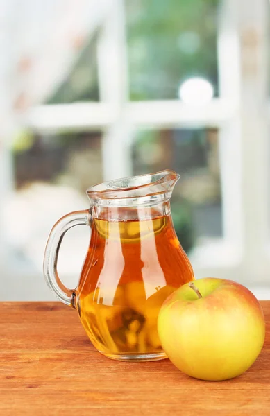 stock image Full jug of apple juice and apple on wooden table on bright background