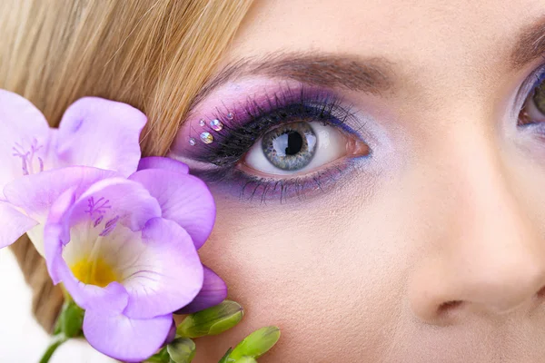 Mooie vrouwelijke ogen met helder blauwe make-up en bloem — Stockfoto