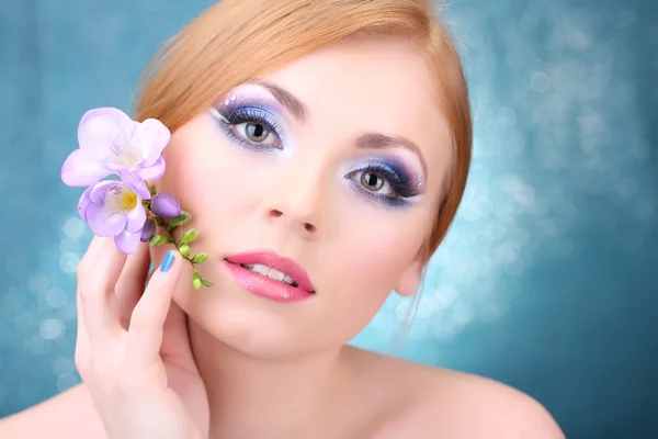 Hermosa mujer joven con glamour maquillaje y flor sobre fondo azul — Foto de Stock