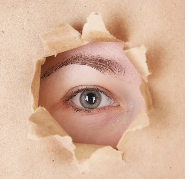 Vrouwelijke oog op zoek door gat in vel papier — Stockfoto