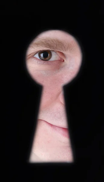Uomo occhio guardando attraverso il buco nel buco della serratura, su sfondo nero — Foto Stock