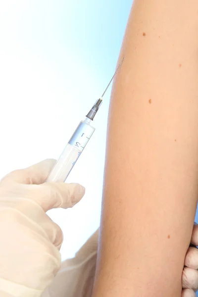 Doktor hospodářství stříkačka očkovací látkou v pacientovi rameno, na modrém pozadí — Stock fotografie