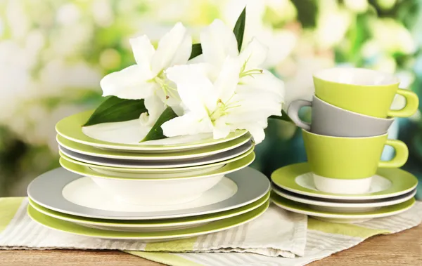 Empty plates and cups on wooden table on green background — Stock Photo, Image