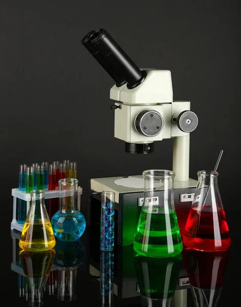 Provette con liquidi colorati e microscopio su fondo grigio scuro — Foto Stock