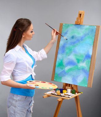 güzel bir genç kadın ressam gri arka plan üzerinde iş başında