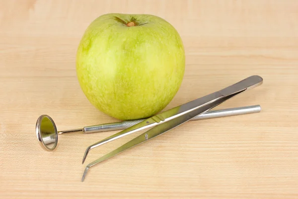 Grüner Apfel und zahnärztliche Instrumente auf hölzernem Hintergrund — Stockfoto