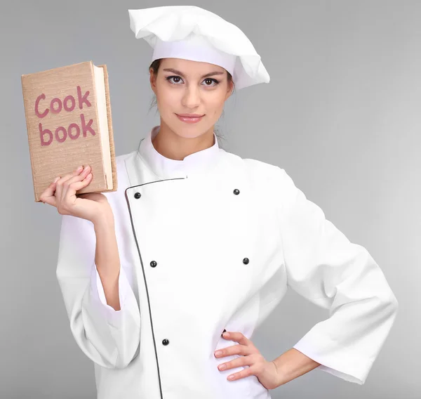 Portrait de jeune femme chef avec livre de cuisine sur fond gris — Photo