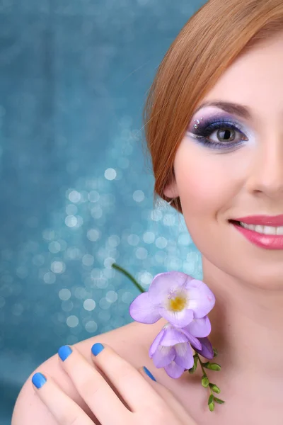 Krásná mladá žena s glamour make-upu a květin na modrém pozadí — Stock fotografie