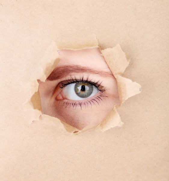 Weibliches Auge blickt durch Loch im Blatt Papier — Stockfoto