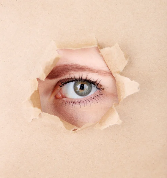 Occhio femminile che guarda attraverso buco in foglio di carta — Foto Stock