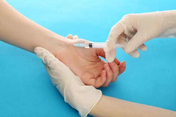 Médico sosteniendo la jeringa con una vacuna en la mano del paciente, sobre fondo azul — Foto de Stock