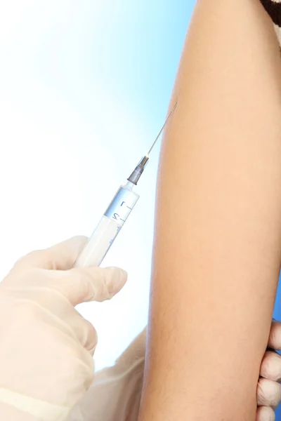 Doctor holding syringe with a vaccine in the patient shoulder, on blue background — Stock Photo, Image