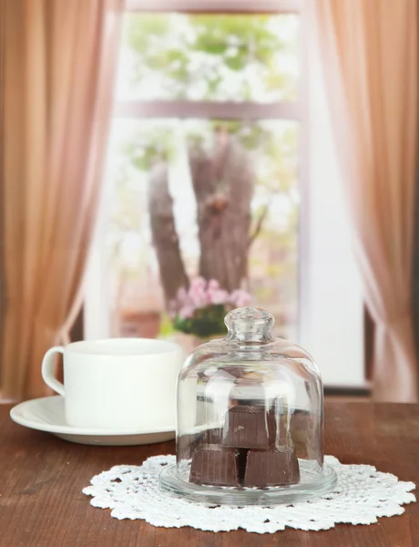 Doces de chocolate sob tampa de vidro e bebida quente em fundo brilhante — Fotografia de Stock