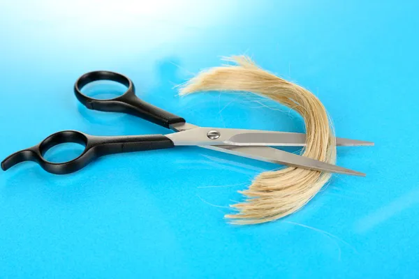 Pedaços de cabelo cortados com tesoura em fundo azul — Fotografia de Stock