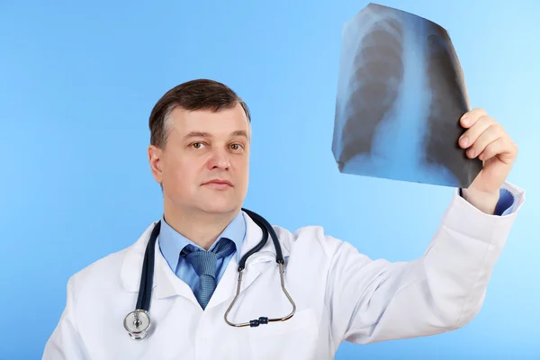 Médico analizando imagen de rayos X sobre fondo azul — Foto de Stock