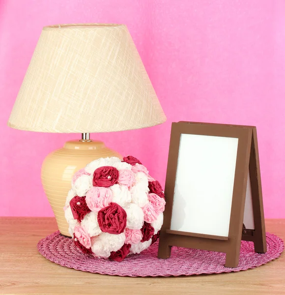 Marco de fotos marrón y lámpara sobre mesa de madera sobre fondo de pared rosa — Foto de Stock