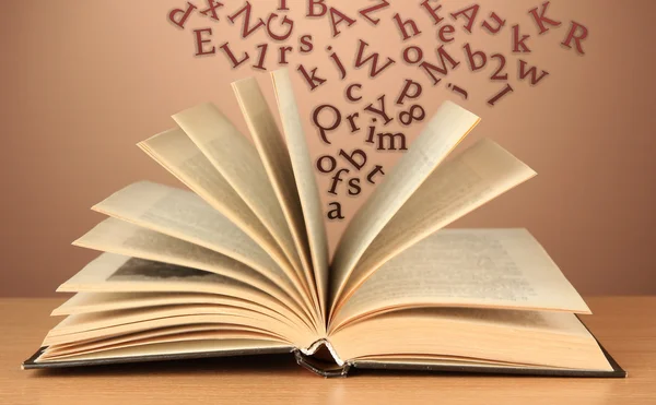 Открытая книга с буквами, вылетающими из нее на коричневом фоне — стоковое фото