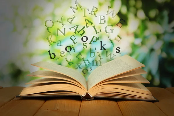 Aufgeschlagenes Buch mit herausfliegenden Buchstaben auf hellem Hintergrund — Stockfoto