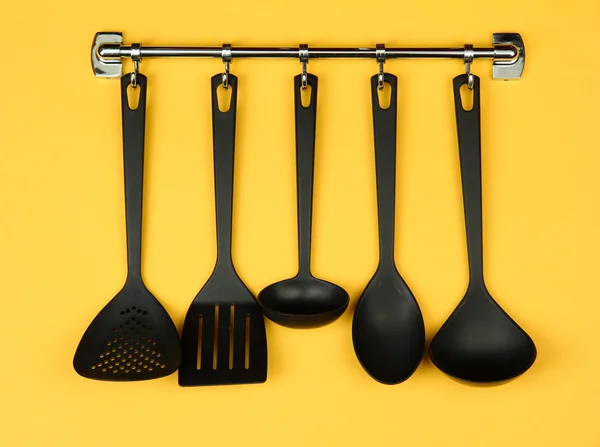 Black kitchen utensils on silver hooks, on yellow background — Stock Photo, Image