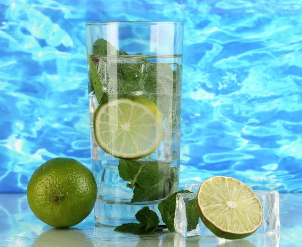 Bicchiere d'acqua con ghiaccio, menta e calce su fondo marino — Foto Stock