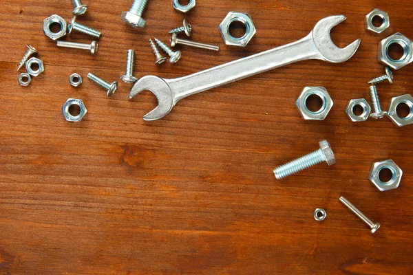 Śruby, wkręty, nakrętki i klucz na drewnianym stole — Zdjęcie stockowe
