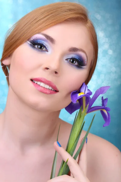 Hermosa mujer joven con glamour maquillaje y flor sobre fondo azul — Foto de Stock