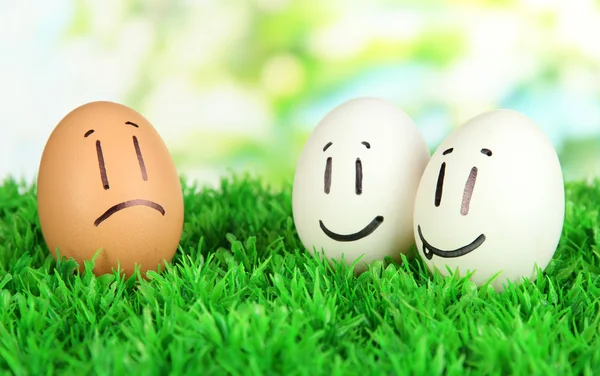 Eggs with funny faces on grass on bright background — Stock Photo, Image