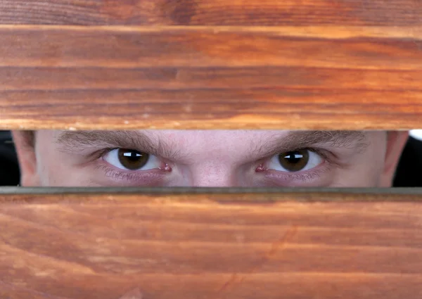 Hombre ojos mirando a través de agujero en escritorio de madera —  Fotos de Stock