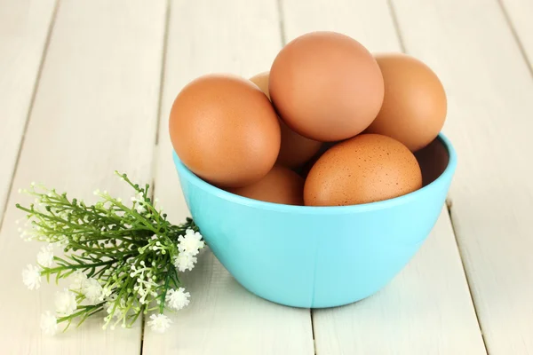 Яйца в синей миске на деревянном столе крупным планом — стоковое фото