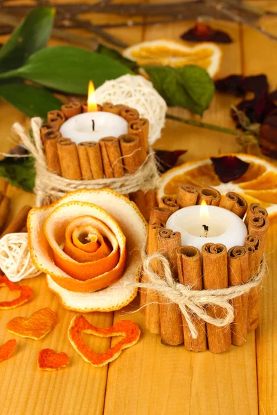 Декоративная роза из сухой апельсиновой кожуры и горящие свечи на деревянном столе — стоковое фото
