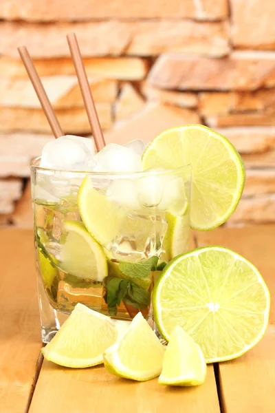 Glass of cocktail with lime and mint on wooden table on stone wall background — Stock Photo, Image