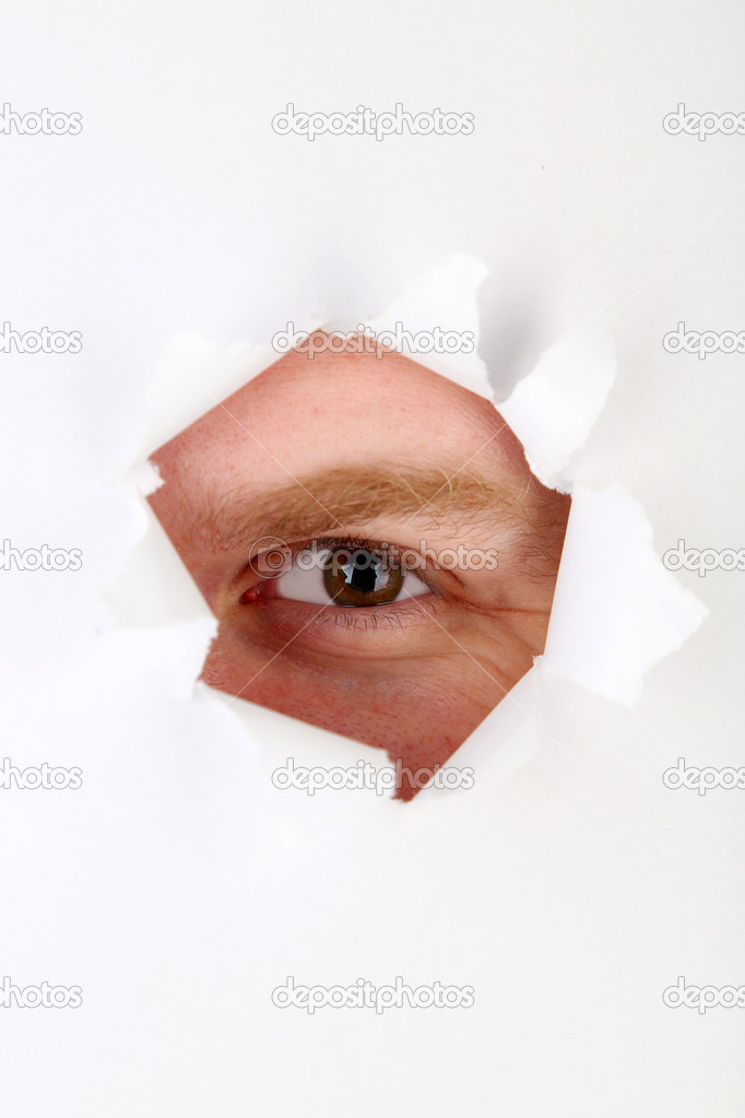 Man eye looking through hole in sheet of paper