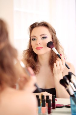 Genç ve güzel bir kadın aynanın yanında makyaj yapıyor.