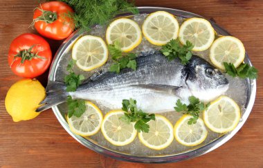 dorado fresco en tajadera con limón y verduras en la mesa de madera