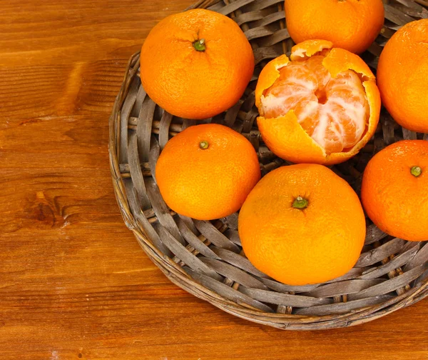 Tasty mandarines on wicker mat on wooden background — Stock Photo, Image