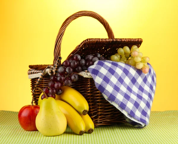 Cesta de picnic con frutas sobre tela sobre fondo amarillo — Foto de Stock