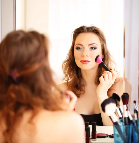 Jovem bela mulher fazendo maquiagem perto do espelho — Fotografia de Stock